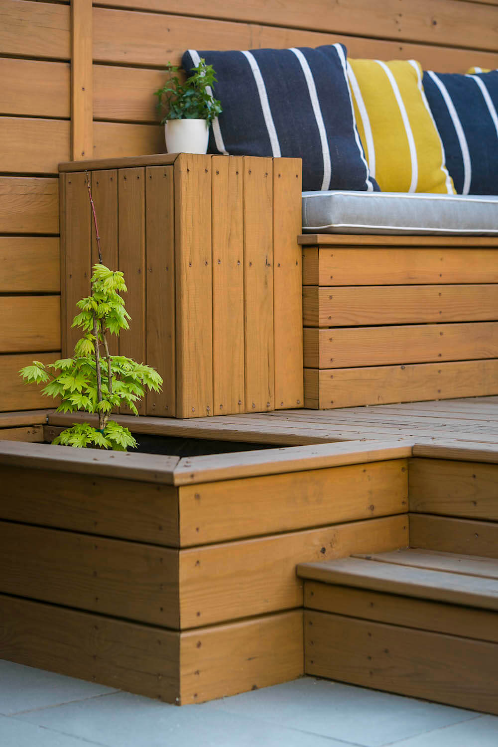 Brown planters with plants and in built seating below the deck after renovation