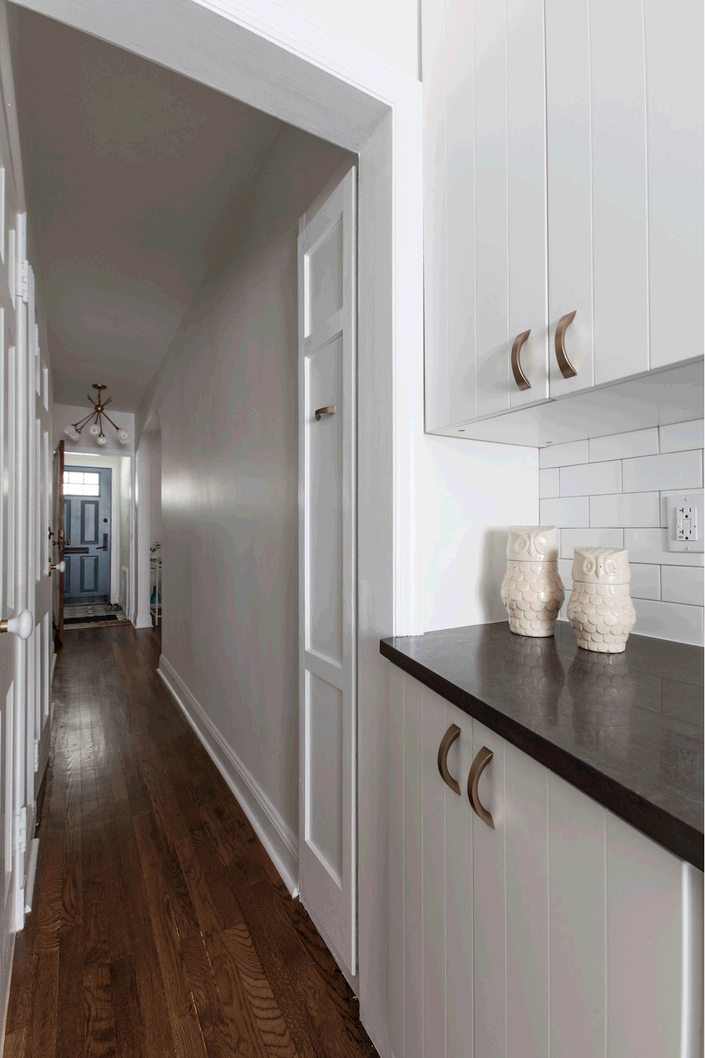 white kitchen cabinets and granite countertop and white backsplash in a wooden floored kitchen towards passageway after renovation