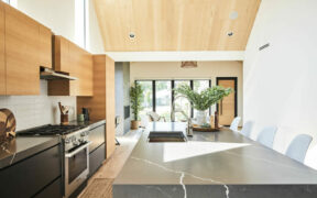 gray dining table in a room with open kitchen with black kitchen cabinets and overhead wooden kitchen cabinets after renovation