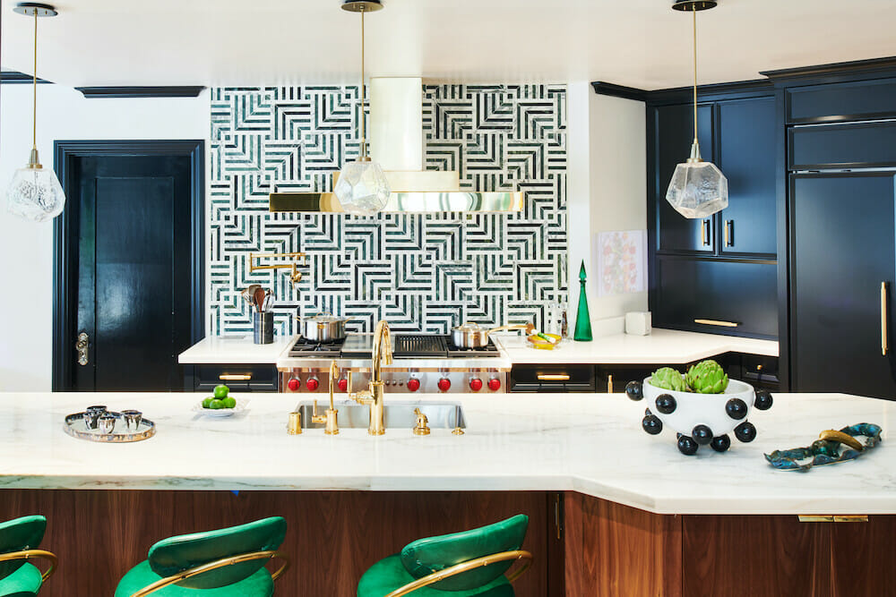 peninsula island in kitchen with white marble countertop and undermount sink with gold faucet and fixtures and pendant lights and black kitchen cabinets and geometric pattern black white backsplash tiles and vent over cooking range after renovation
