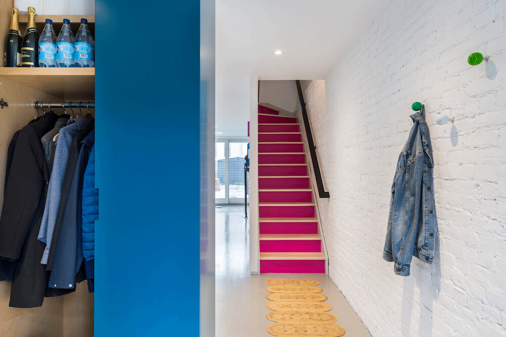 View of pink staircase with railing and white wall with green coat hanger hooks