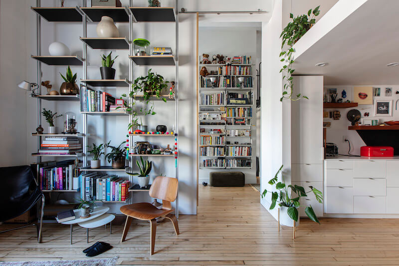 library next to kitchen with hardwood floors and partition wall to living room and floor to ceiling built-in industrial shelves and white walls after renovation