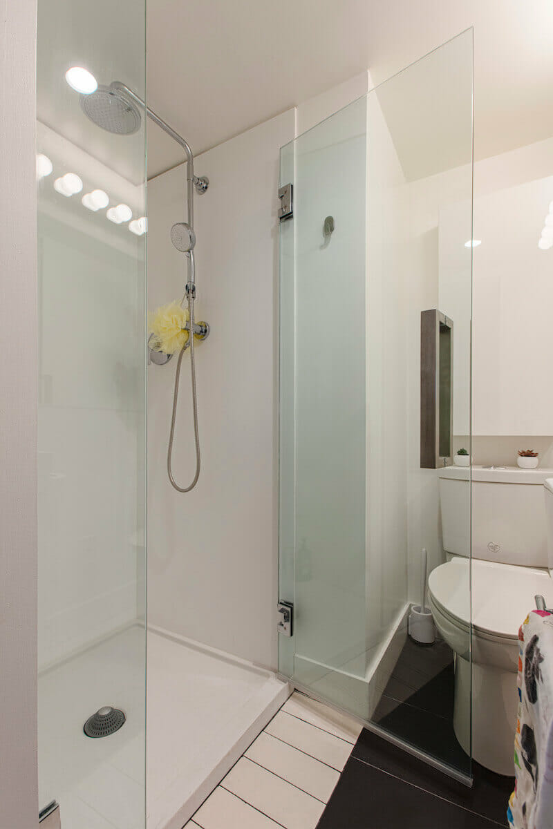 Walk in shower with glass door and bathroom mirror with toilet before renovation