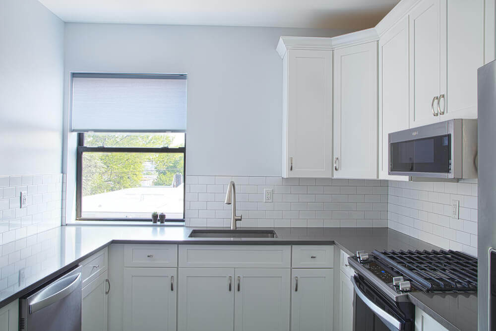 White kitchen cabinetry with black granite countertop and double hung window after renovation