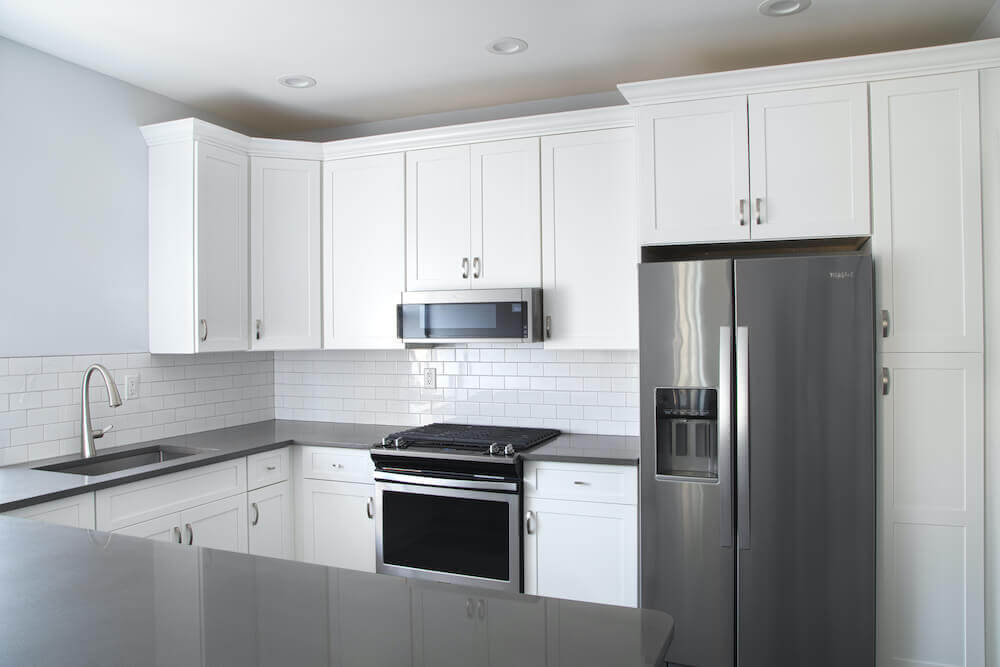 White kitchen with granite countertop along with double door fridge after renovation