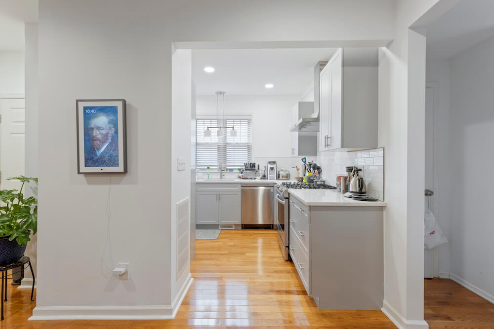 Entryway to a white kitchen and white cabinetry with wooden flooring after renovation