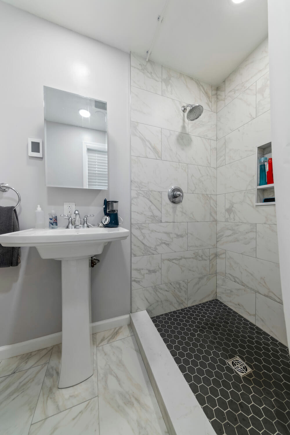 White bathroom with walk in shower along with a pedestal washbasin and a rectangle bathroom mirror