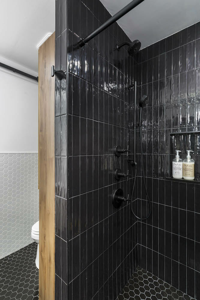 Black shower rod in an all black shower space with hexogon floor tiles after renovation