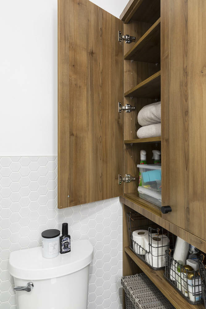 Open natural wood cabinet with toiletry and white hexogan wall tiles after renovation