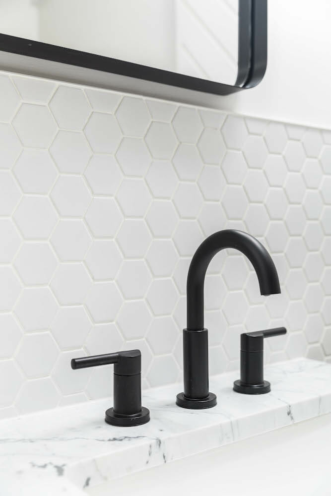white honeycomb or hexagon wall tiles and white marble on vanity with black faucet and fixtures after renovation