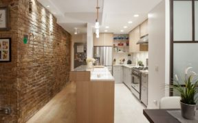 brown brick wall in passageway with open kitchen and white kitcben cabinets after renovation