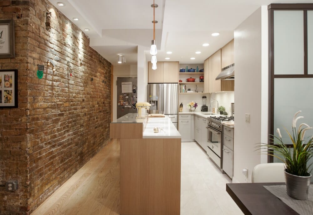 brown brick wall in passageway with open kitchen and white kitcben cabinets after renovation