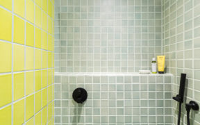 walk-in shower with sage green square tiles on two walls and yellow tile on an other wall and black shower fixtures after renovation