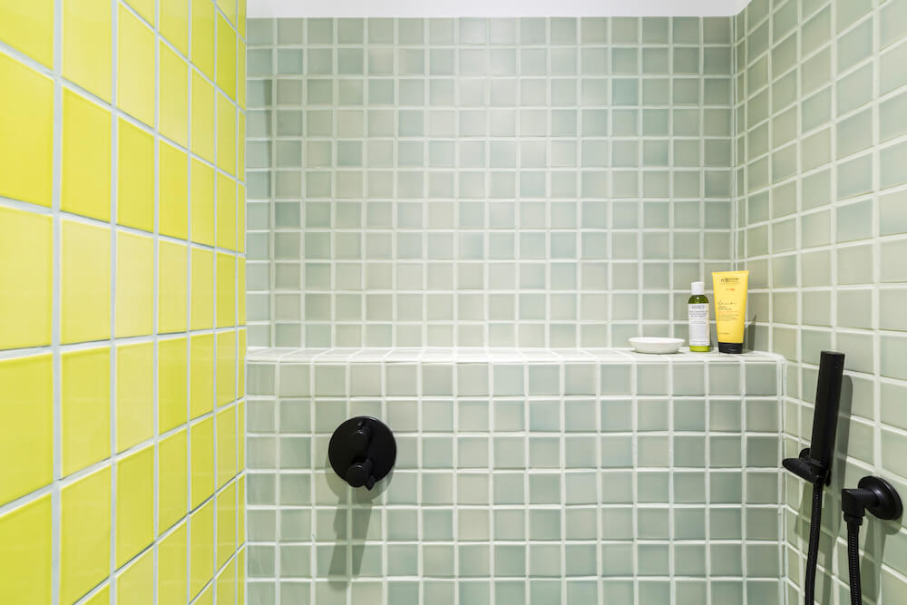 walk-in shower with sage green square tiles on two walls and yellow tile on an other wall and black shower fixtures after renovation