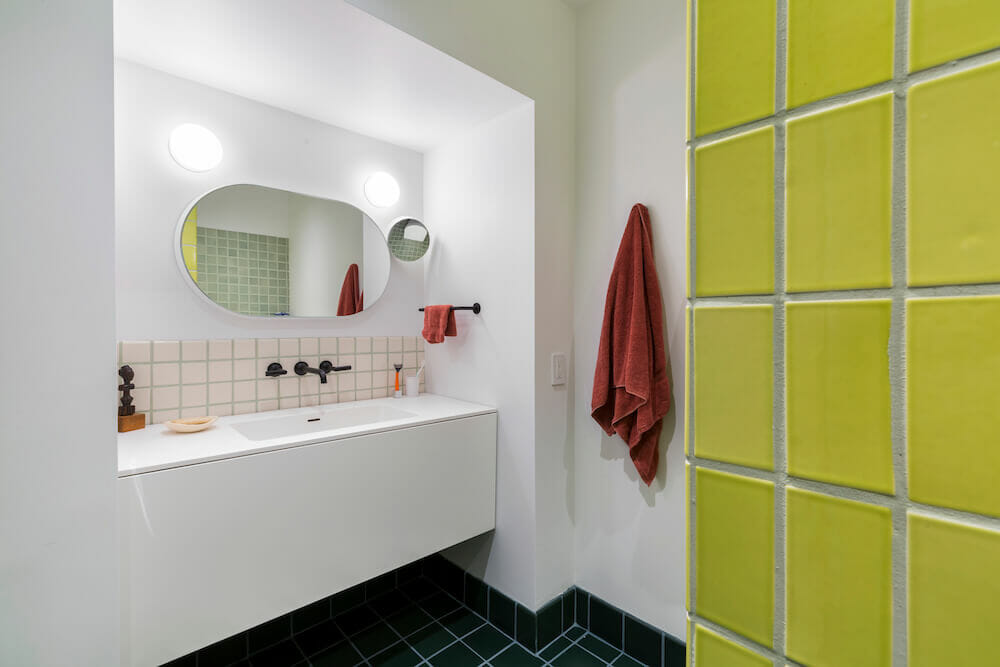 White bathroom with yellow wall tile and oval mirror over a white sink after renovation
