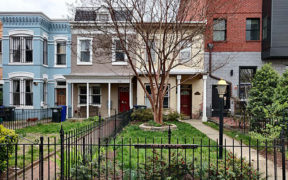 row houses with porch and red front door and landscaped front yard with black metal fence after renovation