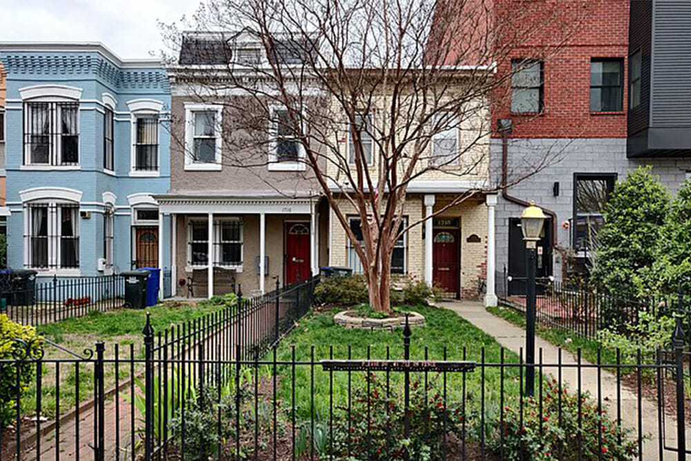 row houses with porch and red front door and landscaped front yard with black metal fence after renovation