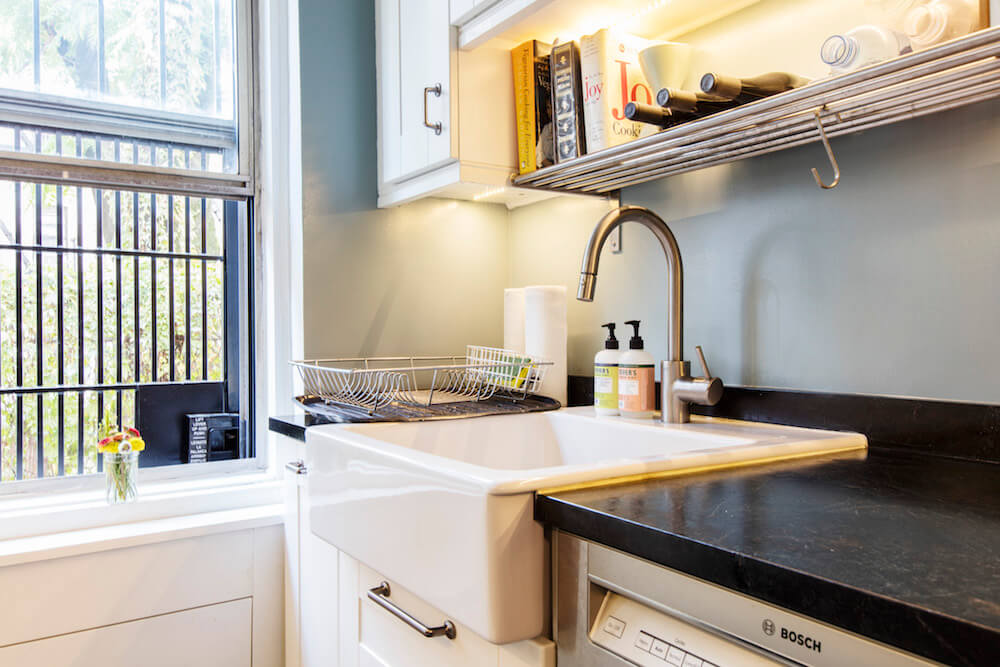 white kitchen cabinets with black granite countertop and porcelain farmhouse sink with brushed nickel faucet near window after renovation