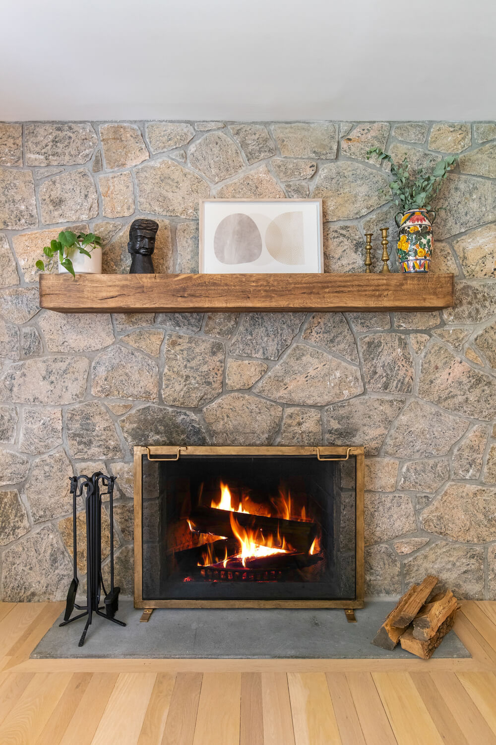 stone fireplace with wooden mantel and brushed brass frame and concrete hearth and hardwood flooring after renovation 