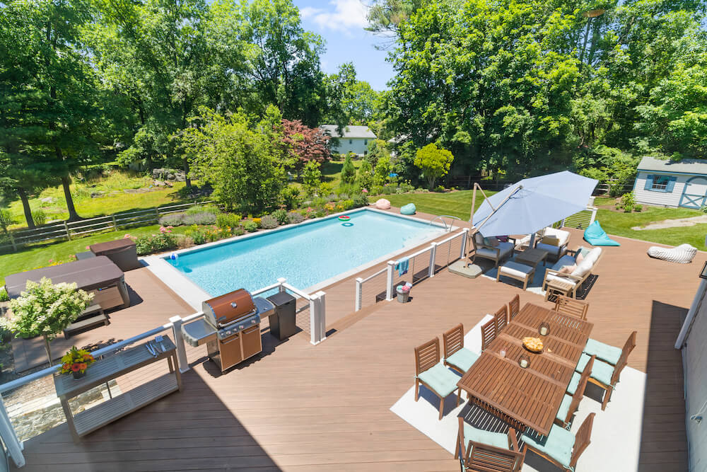 large wooden patio and swimming pool with wooden deck and cable railing dividing patio and deck after renovation