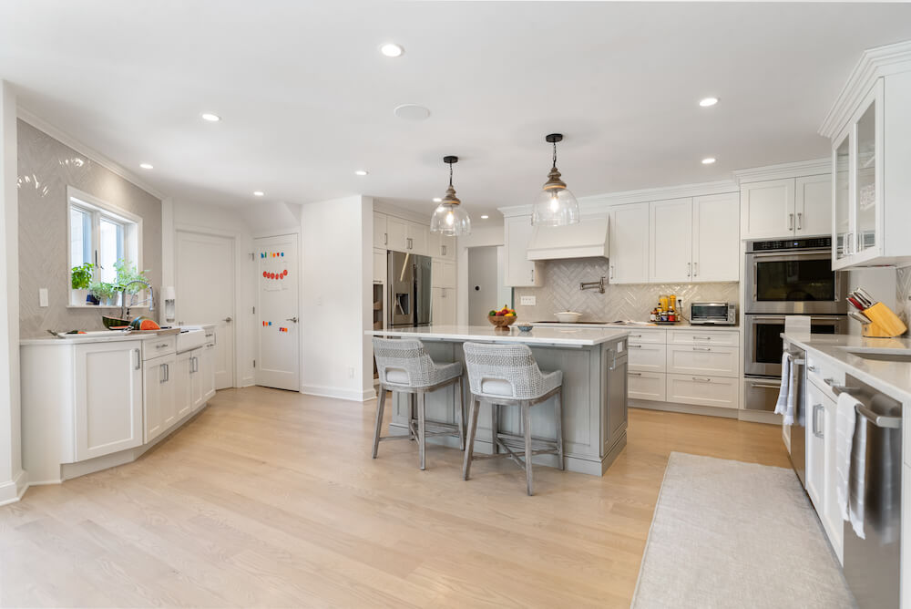 white kitchen cabinets with stainless steel appliances and island with pendant lights and hardwood floors and recessed lights after renovation
