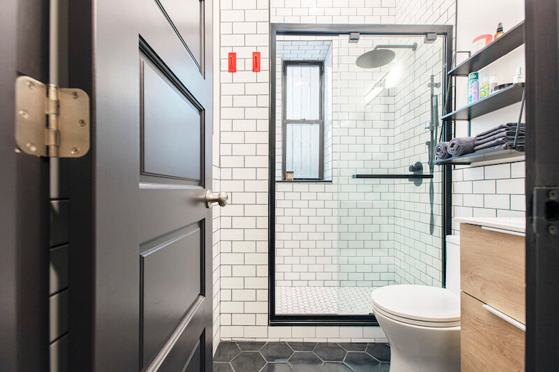 black and white bathroom with subway tiles and black honeycomb or hexagon floor tiles and vanity and walk-in shower after renovation