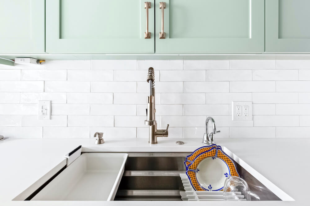 Sea green cabinets with white backsplash and kitchen sink with faucet after renovation