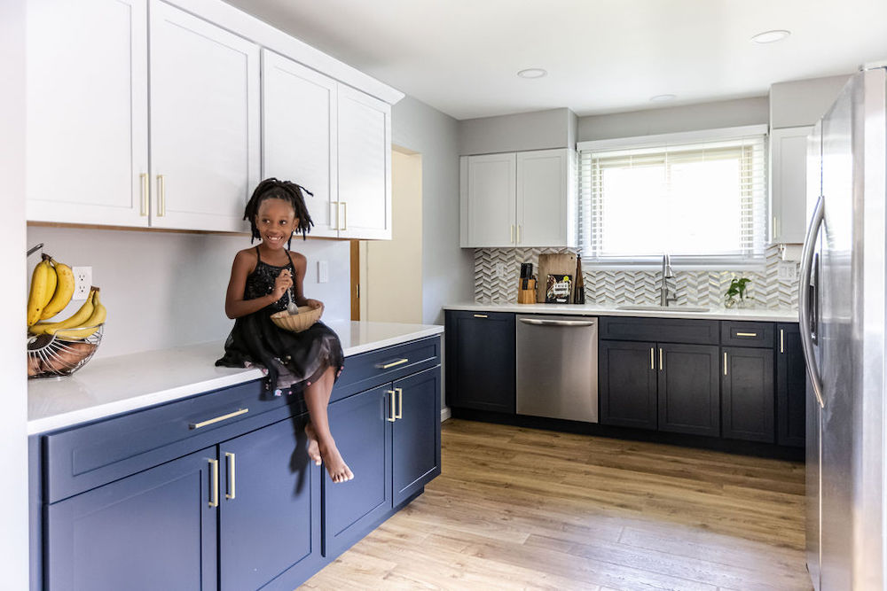 White and blue modern kitchen with little girl sitting on the quartz countertop after renovation
