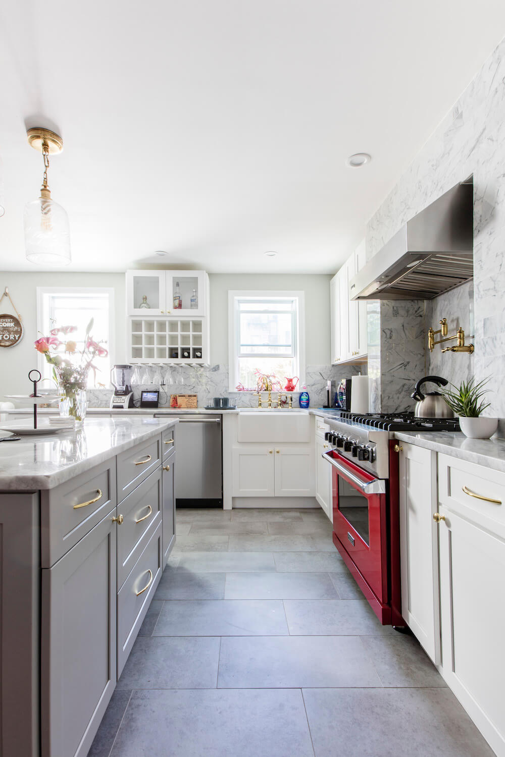 White kitchen with kitchen island and bright red cooking range over light gray floor tile after renovation