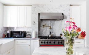 white kitchen cabinets with marble backsplash and countertop and gas range with hood and island with marble countertop and recessed lighting after renovation