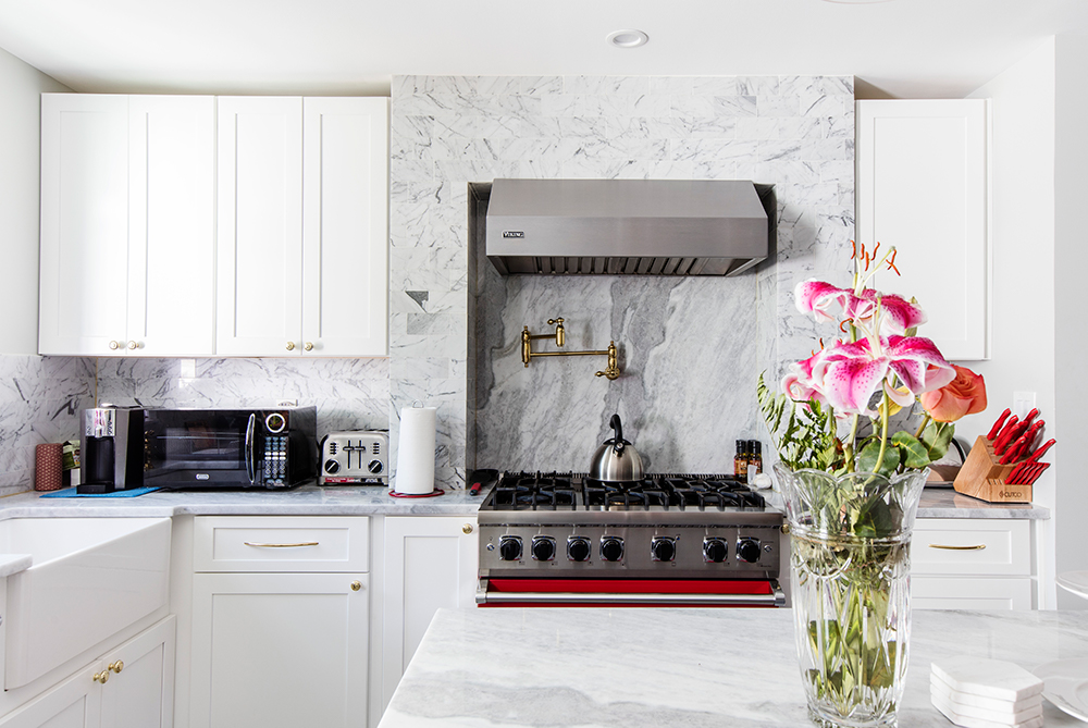 white kitchen cabinets with marble backsplash and countertop and gas range with hood and island with marble countertop and recessed lighting after renovation