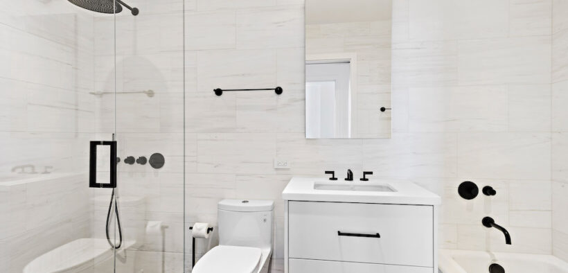 Small white bathroom with glass separator for walk-in shower and bathroom vanity with mirror after renovation