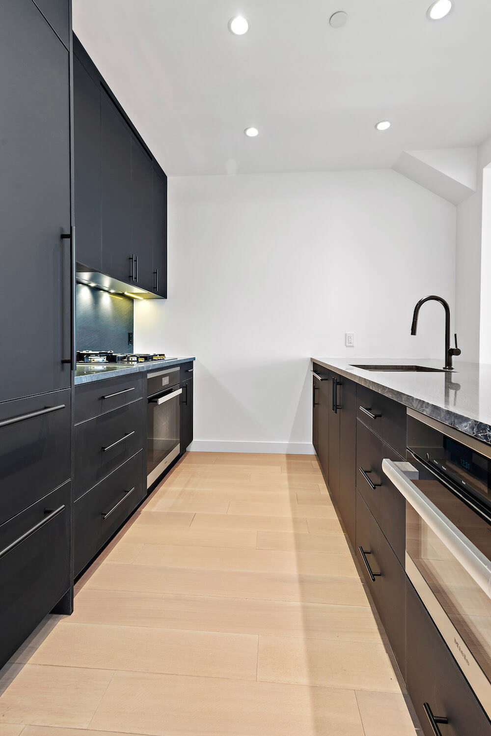 black kitchen cabinets and black stainless steel appliances and under cabinet lighting and peninsula island with undermount sink and black faucet and hardwood floors and recessed ceiling lights after renovation