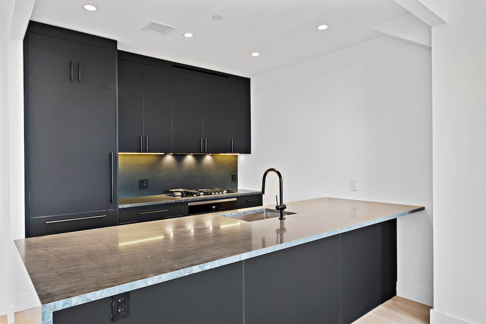 Black kitchen cabinets with kitchen island and recessed light fixtures after renovation