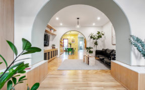 archway to living room with hardwood floors and recessed lights and chandelier and white walls and storage cabinets and archway to dining room with yellow accent wall after renovation