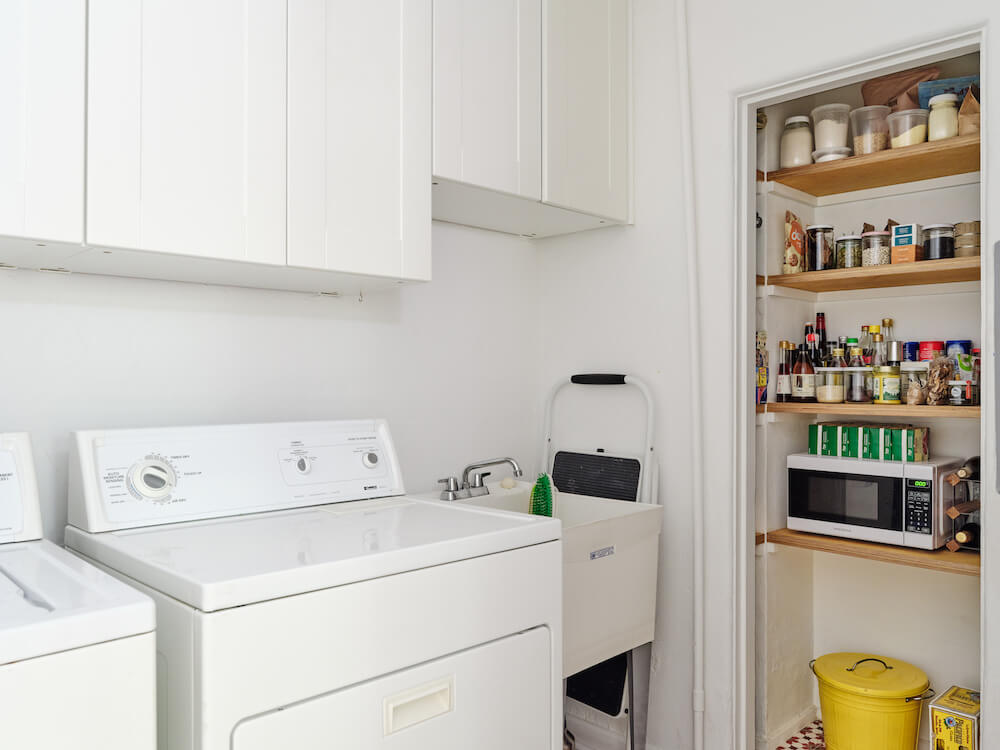 Laundry room with white utility sink, white cabinets and open pantry storage