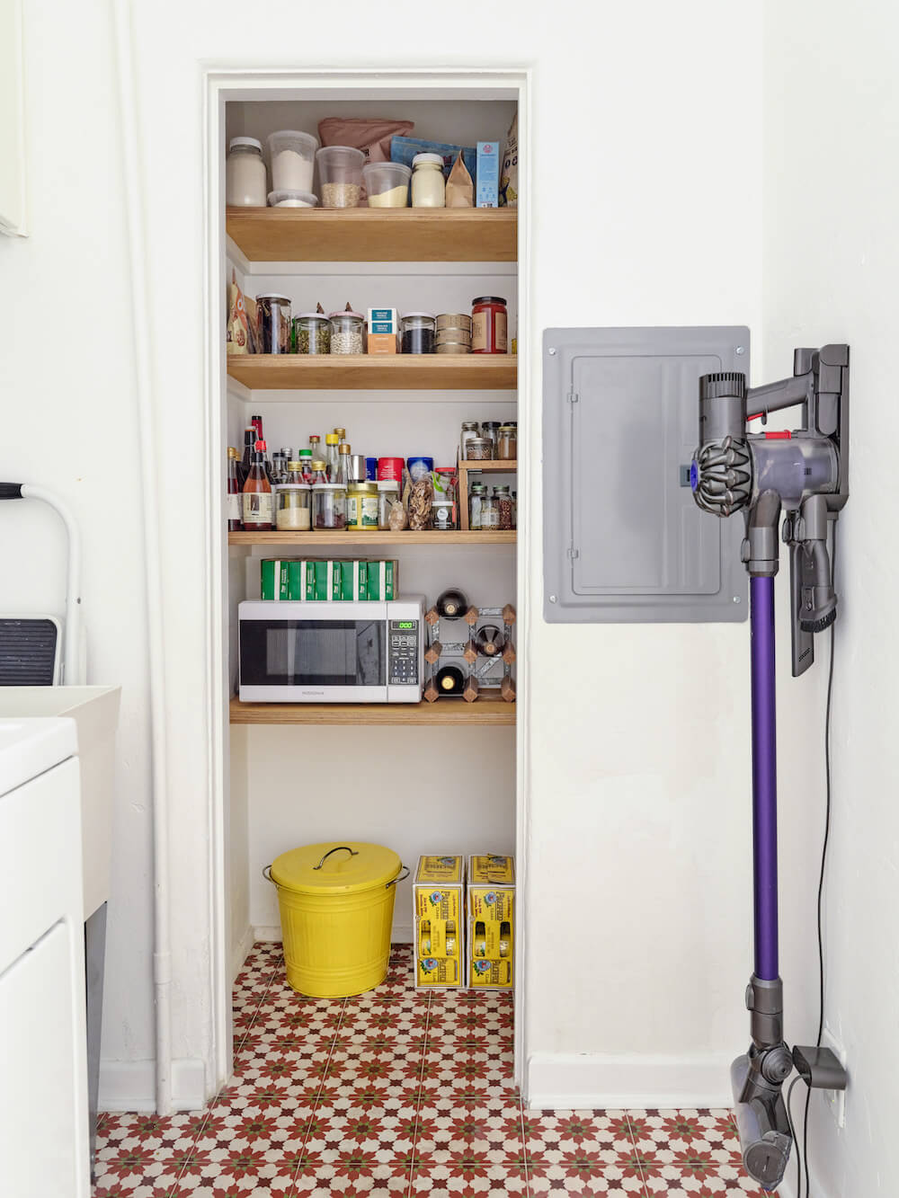 Pantry storage in laundry room with wooden open shelves and microwave storage