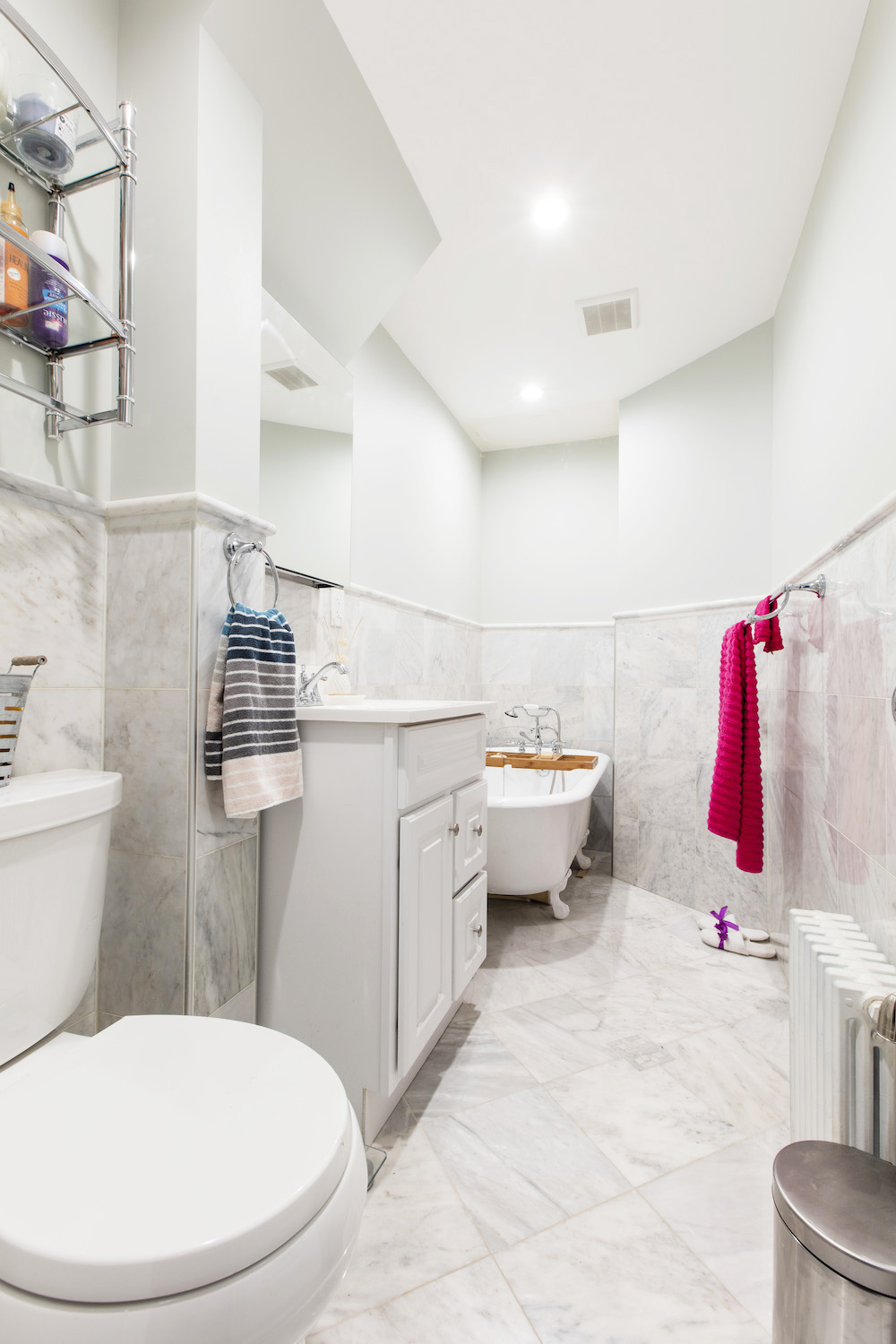 narrow white bathroom with free standing bathtub and vanity and radiator after renovation