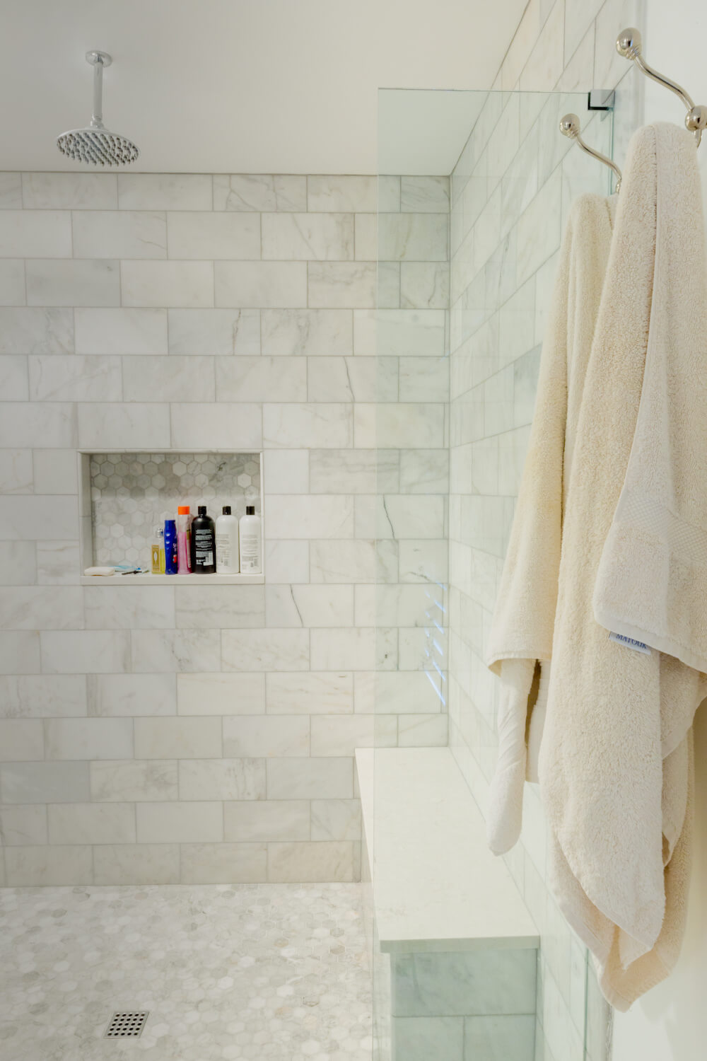 Walk-in shower with white marble tiles and bench seating