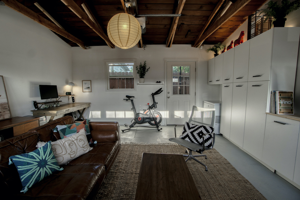 garage converted into a living space with storage cabinets and wooden ceiling with beams and white walls and window and concrete floors after renovation