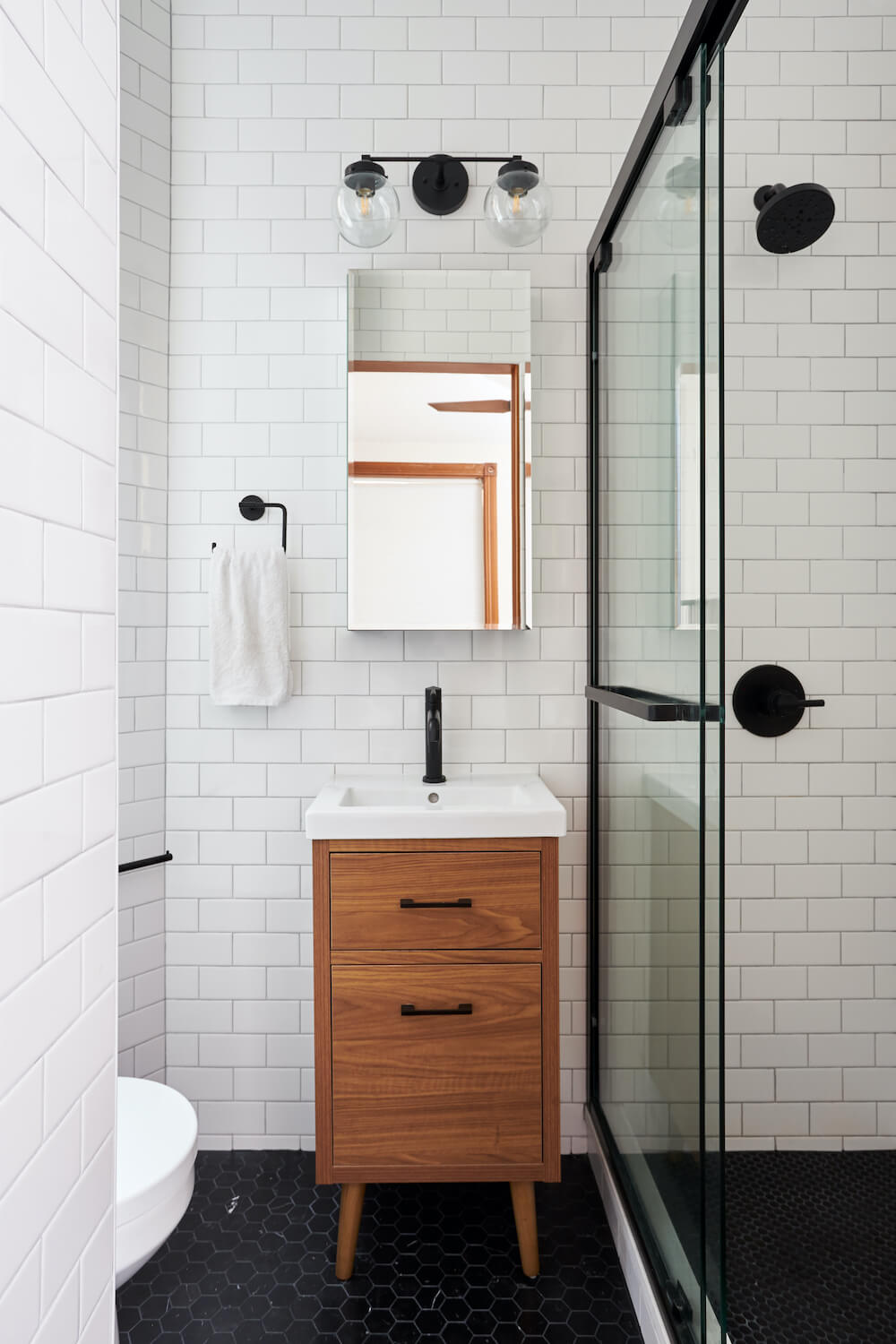 Bathroom with white tiles, black tiled floor, and glass paneled shower