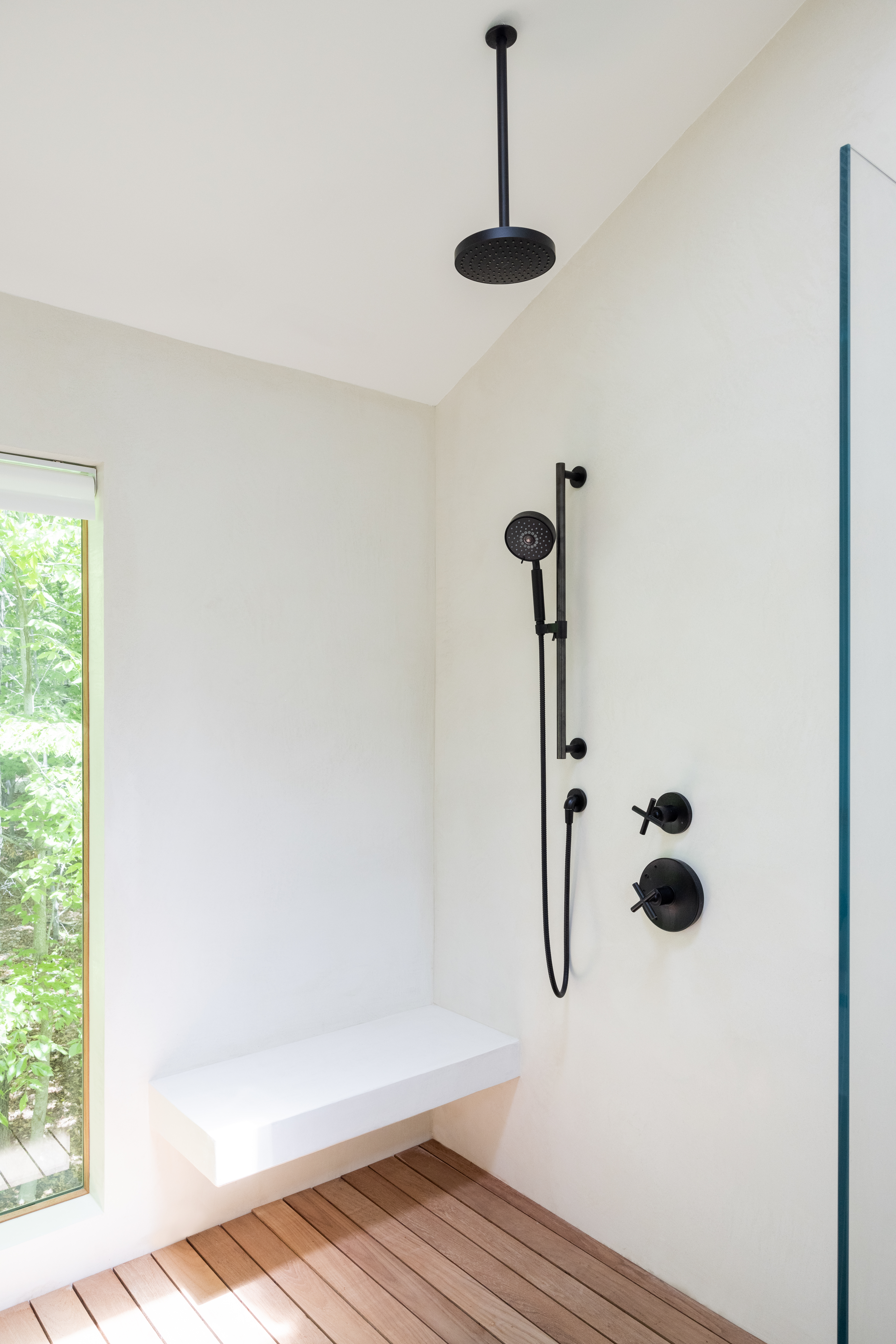Floating shower bench in an Amagansett wet room with tadelakt walls, teak flooring, matte black fixtures, a glass panel, and a picture window.