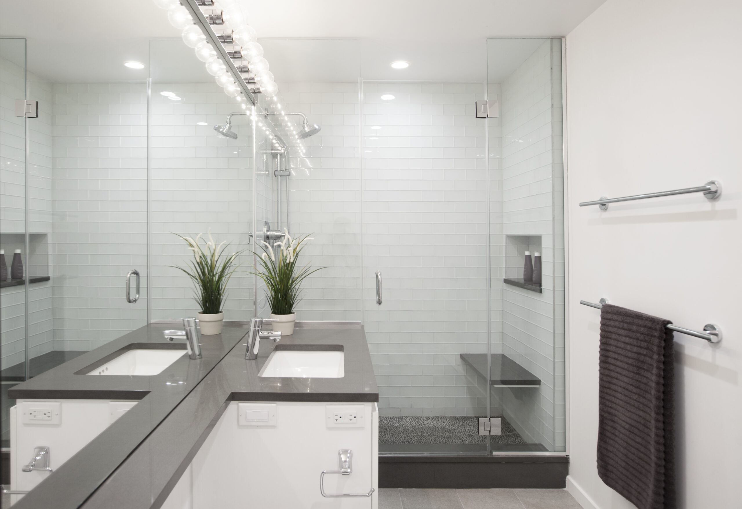 Floating shower bench in a Midtown bathroom with glass enclosure, white subway tile, pebble floor, recessed niches, and a gray vanity countertop.