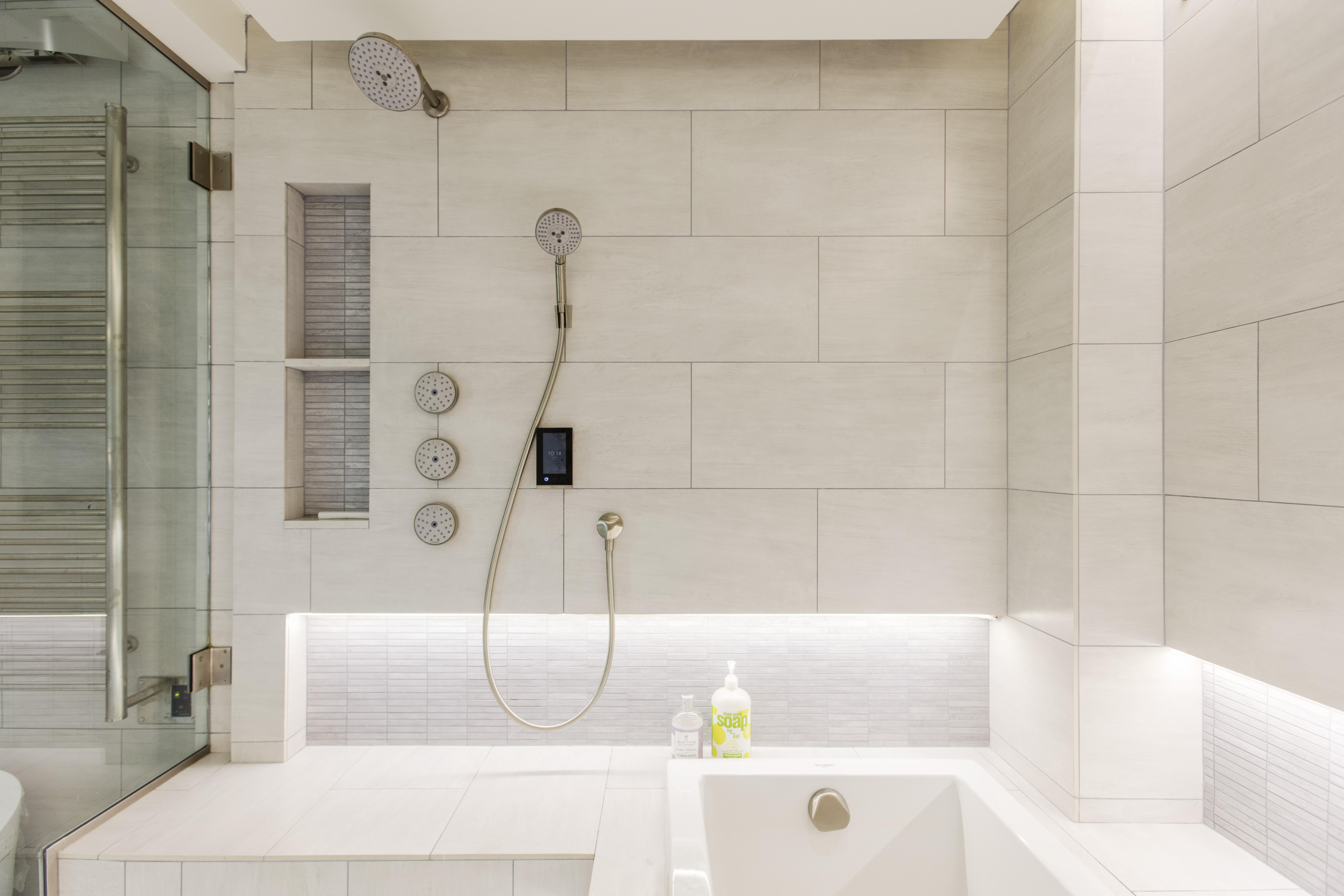 Built-in shower bench in a New York City wet room with large-format tile, recessed storage, handheld fixtures, and integrated lighting along the seat.