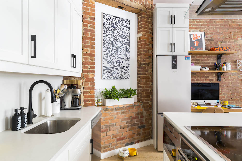 white kitchen with black matte hardware, brick wall and art