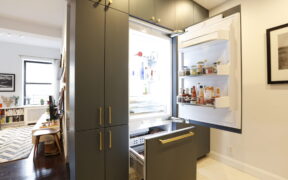 A renovated kitchen featuring gray cabinetry and a hidden fridge cabinet.