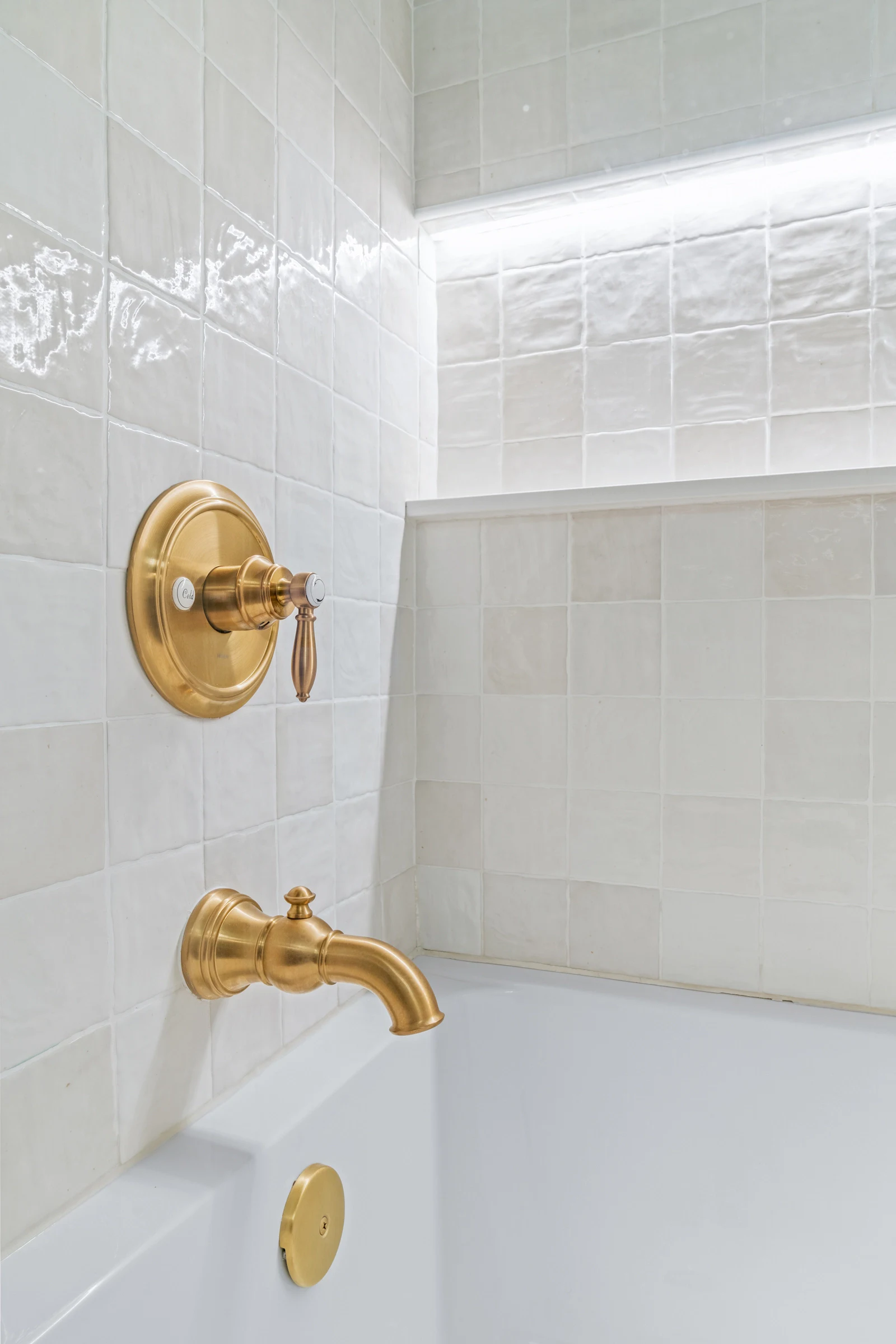 white tub shower textured tile and gold fixtures