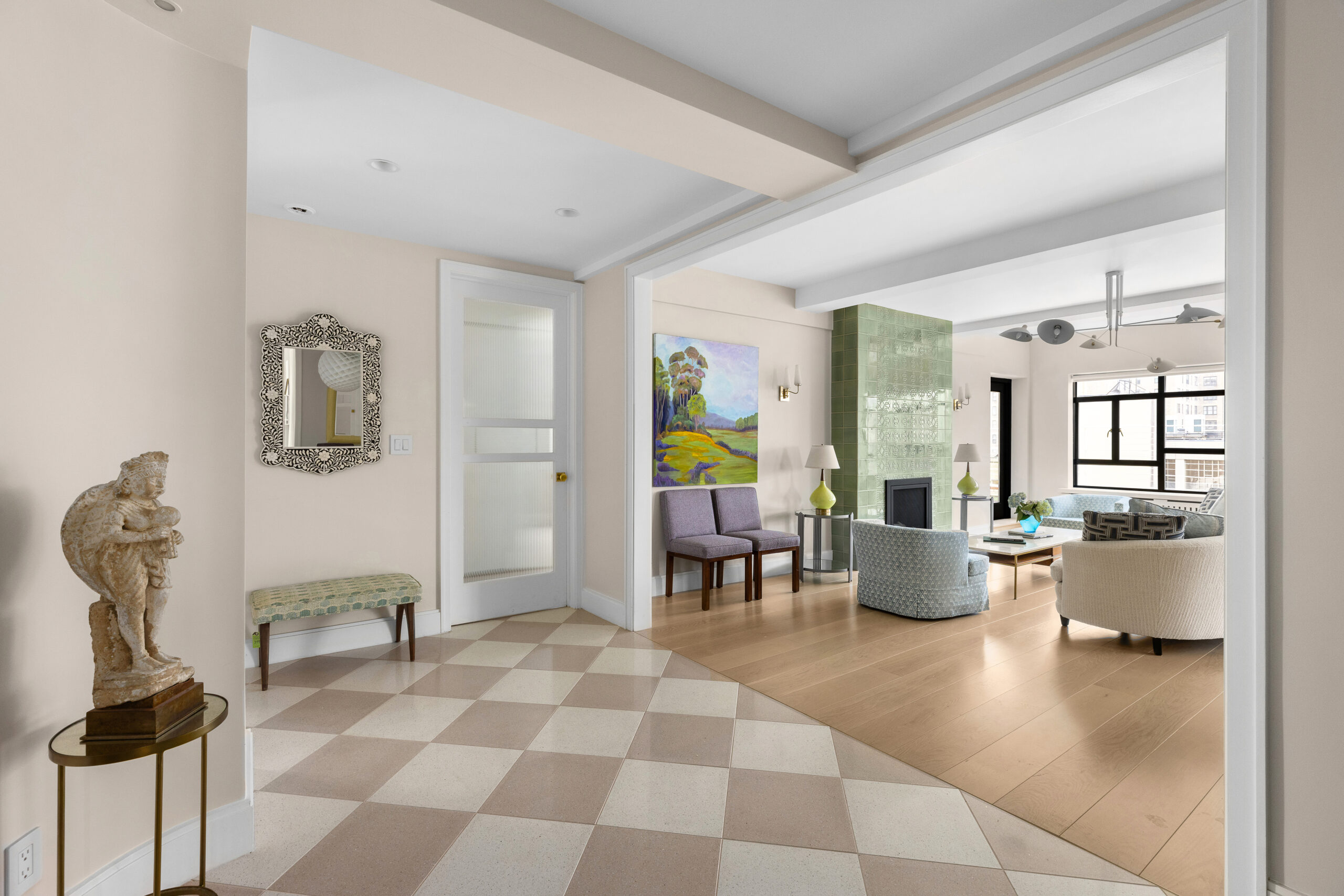 Enlarged foyer with checkered terrazzo floor opens to the remodeled Upper West Side living room with green tiled fireplace and light wood planks.