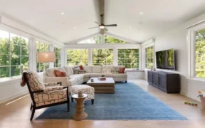 Newly renovated living room with a sofa, blue carpet, flat screen TV, and ceiling fan with light.
