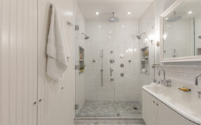 A tub to shower conversion with circular rain showerhead, white wall tile, chrome fixtures, and patterned flooring.